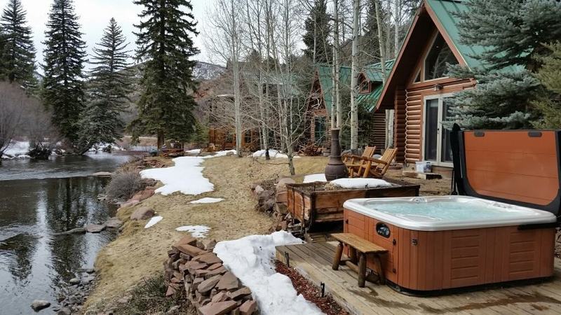 hot tub near wooden house in forest with a river in the background