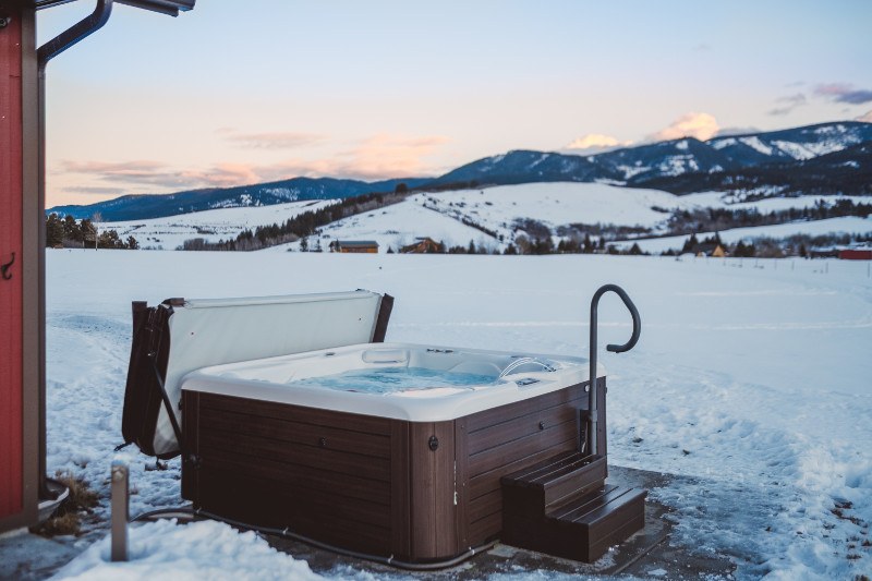 A hot tub on a snowy patio with a mountain view in the background